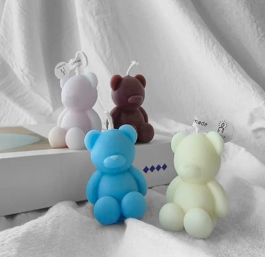Four colorful bear-shaped candles on a white fabric background