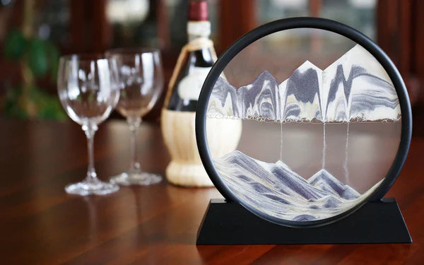 Decorative mountain scene on a stand with wine glasses and a bottle in the background.