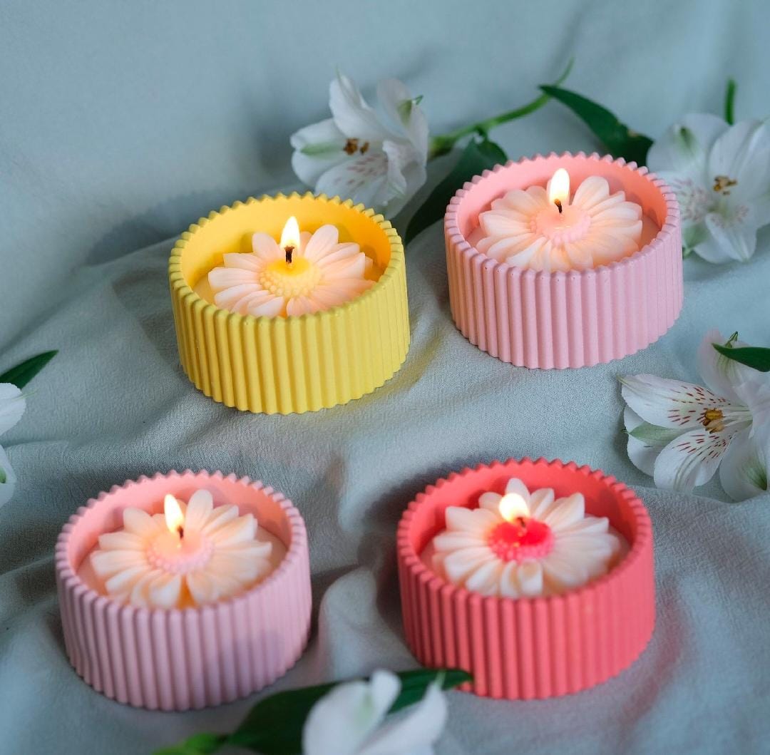 Four floral-patterned candles in yellow, pink, and red holders on a light fabric background with flowers.