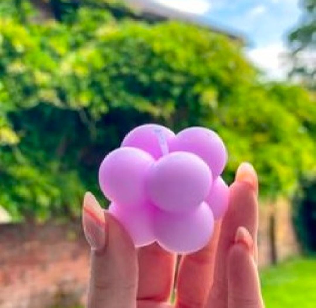 Hand holding a purple stress ball with a blurred green outdoor background
