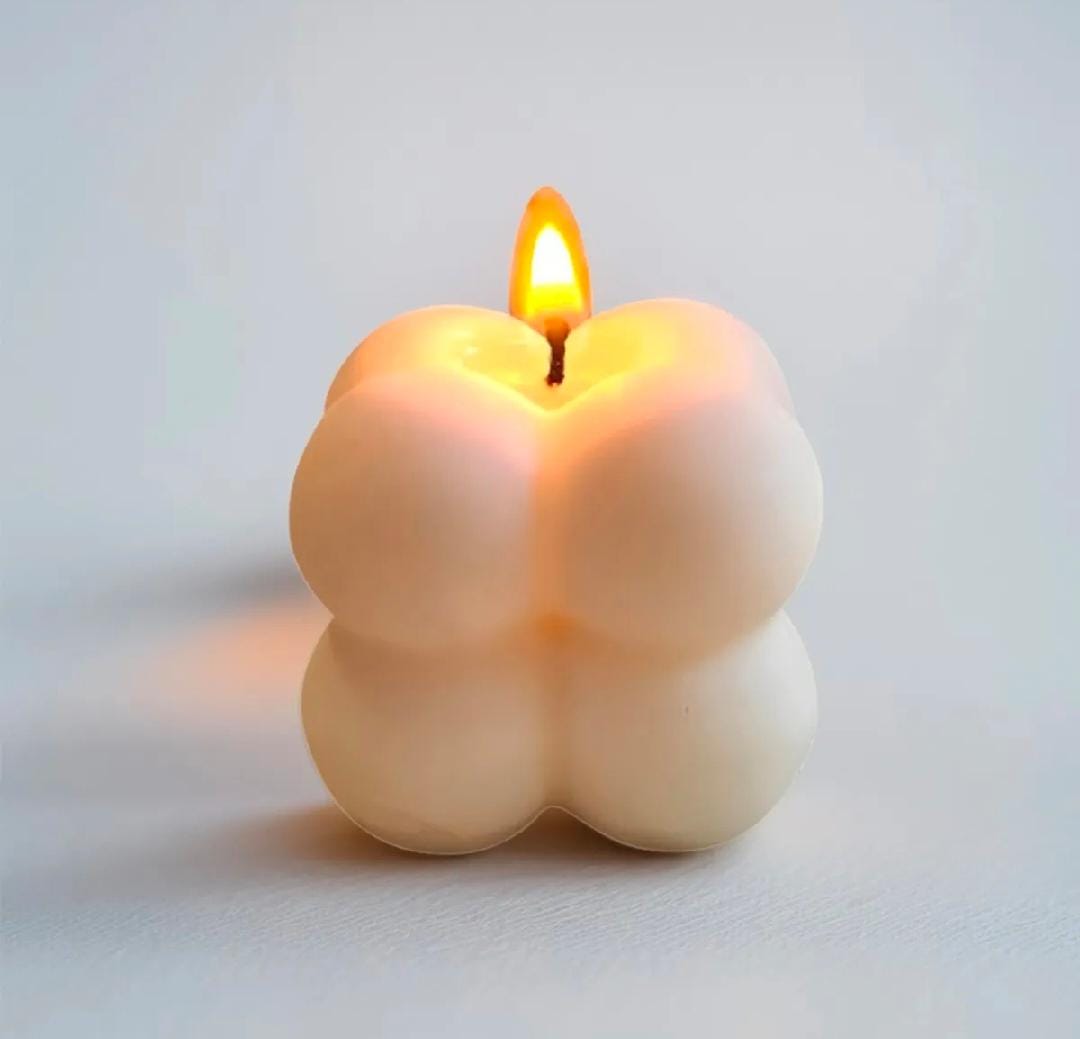 Candle shaped like a peach with a flame on a light gray background