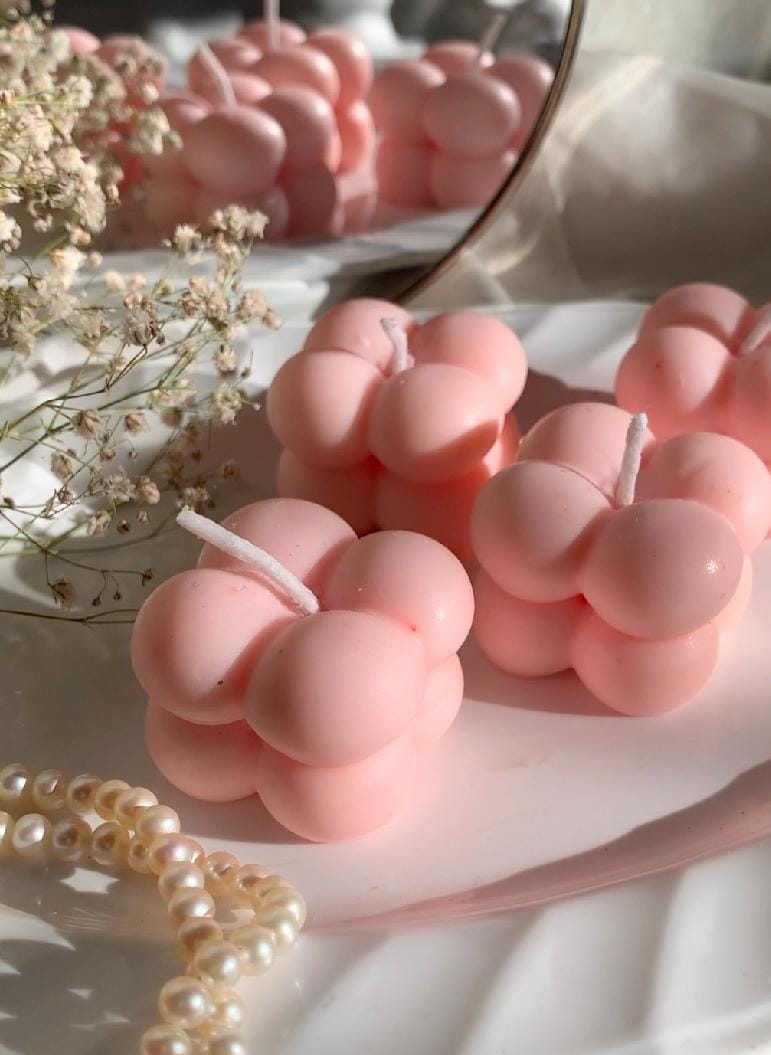 Pink berry-shaped candles on a white surface with a mirror reflection.