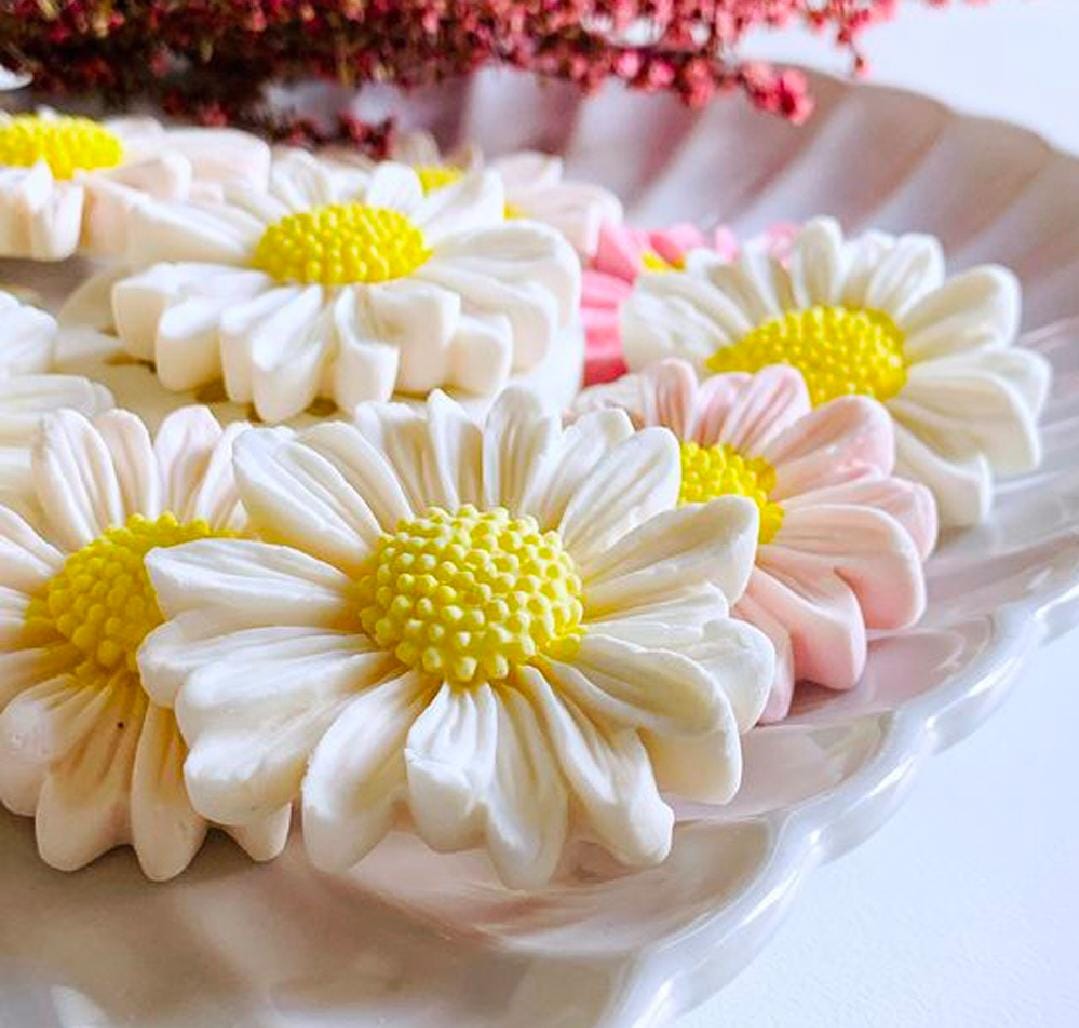 Decorative cookies shaped like daisies with yellow centers on a white plate.