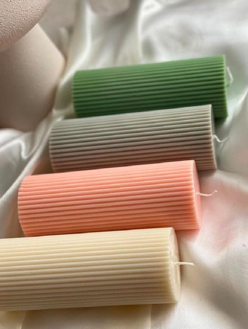 Four cylindrical candles in green, beige, orange, and pink on a textured surface.