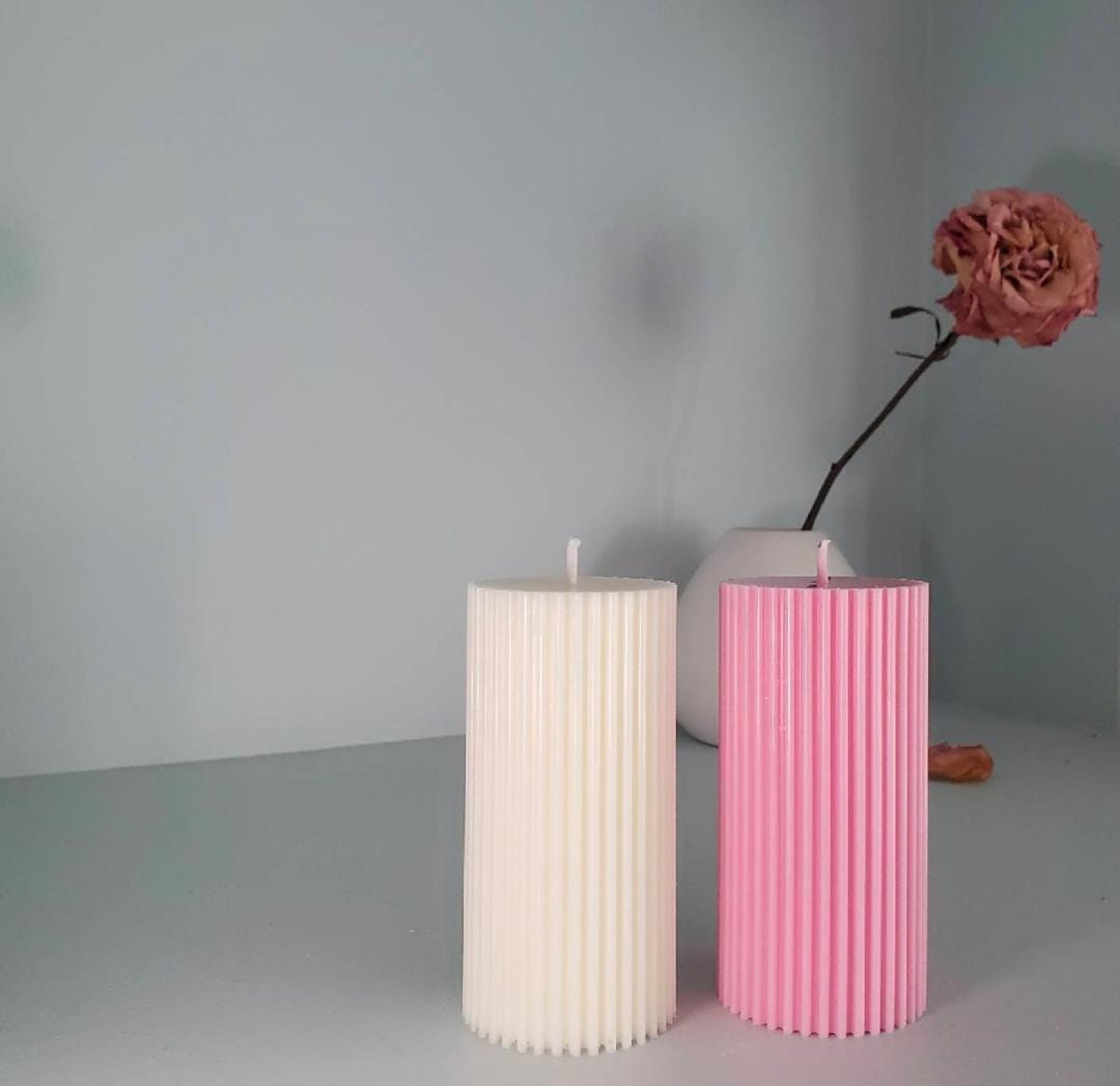 Two ribbed candles, one white and one pink, on a gray surface with a plain background.