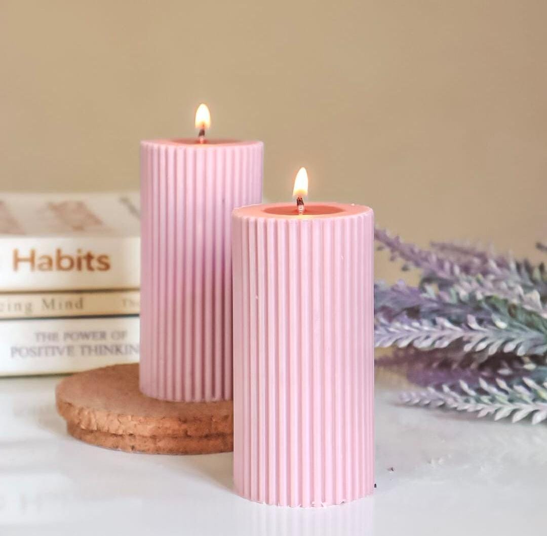Two pink ribbed candles on a cork coaster with books and lavender in the background.