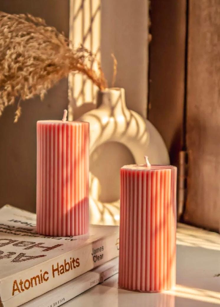 Two ribbed red candles on books with a vase in the background