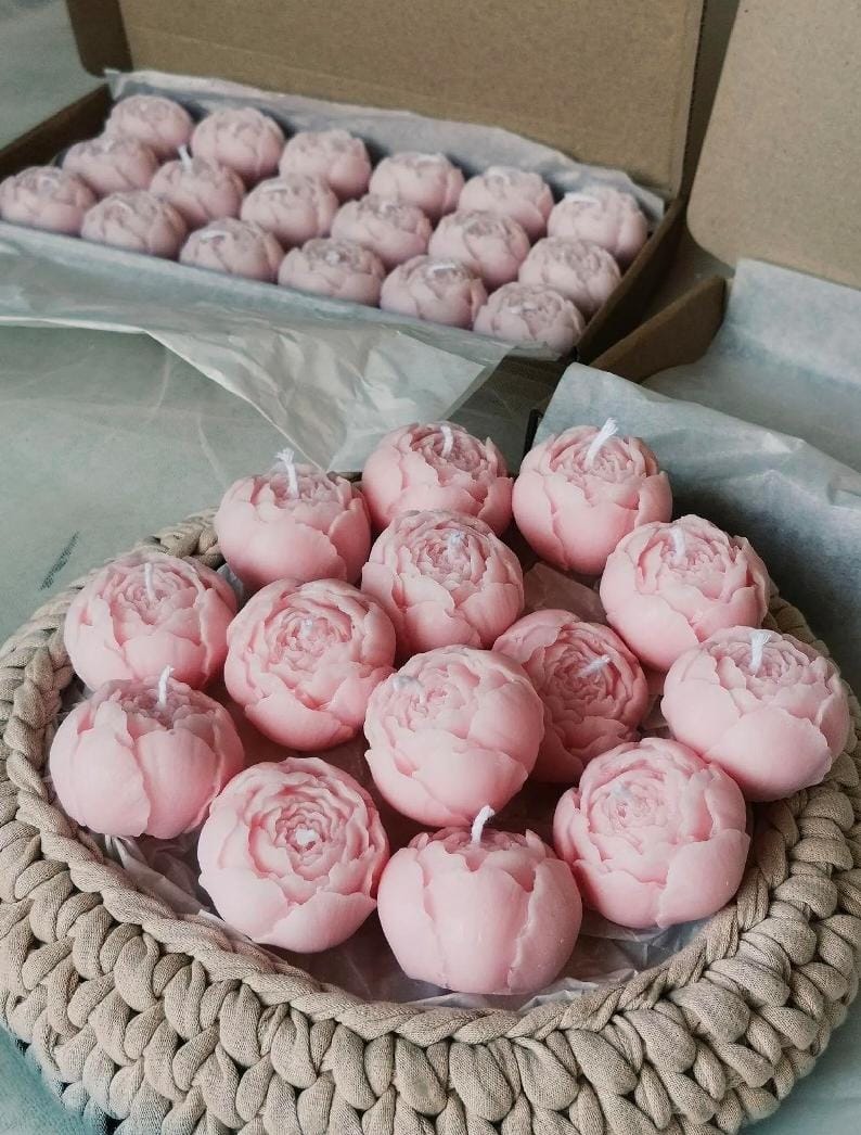 Pink rose-shaped candles on a woven mat with a cardboard box in the background.
