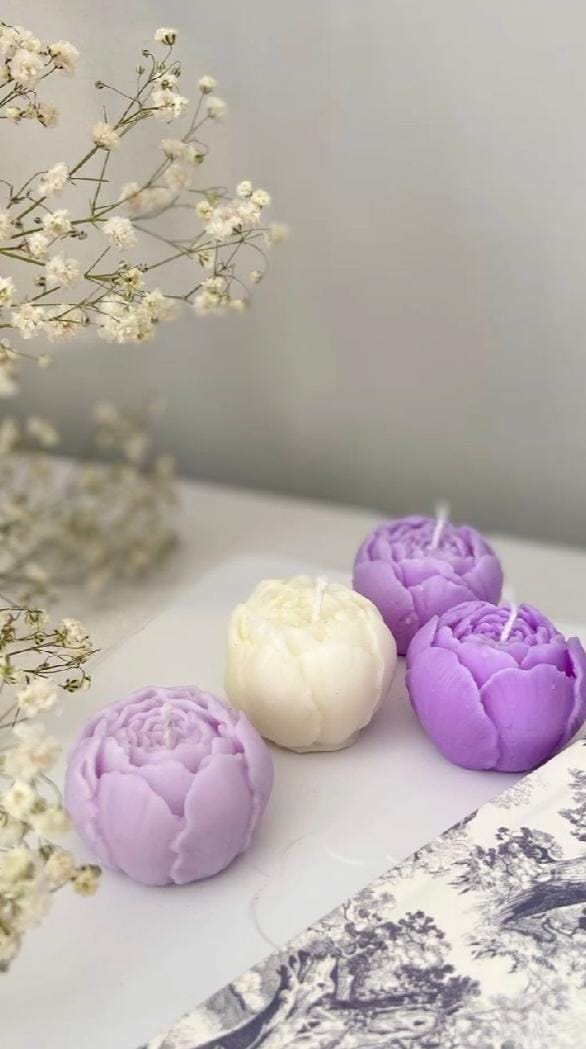 Decorative candles shaped like flowers on a marble surface with flowers in the background