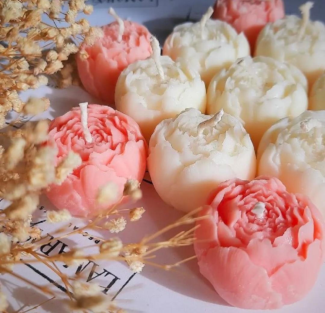 Decorative candles shaped like flowers on a surface with dried flowers.