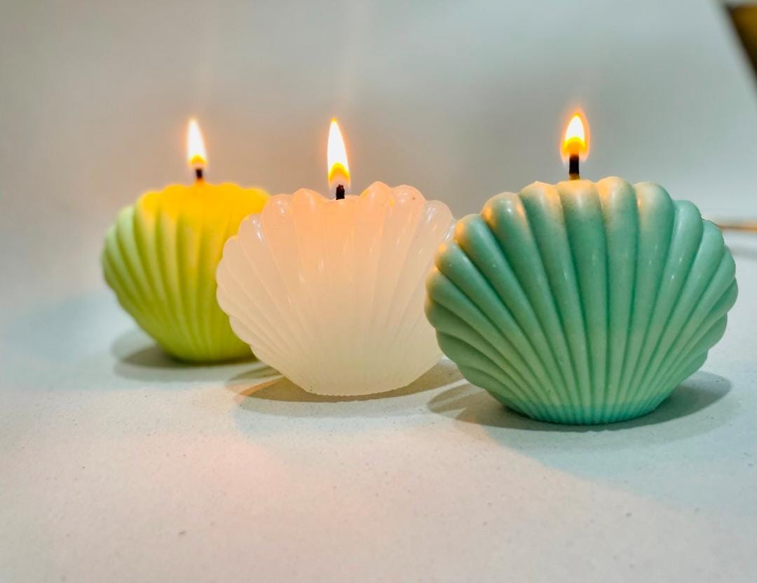 Three shell-shaped candles with lit wicks on a white surface.