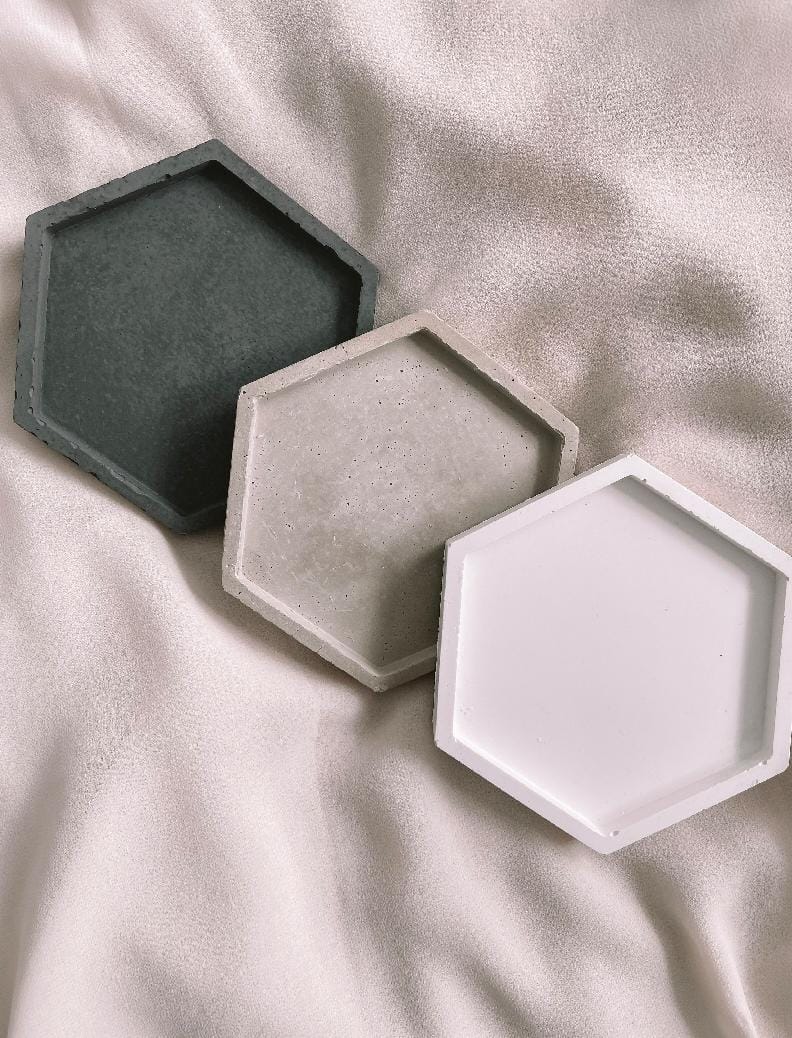 Three hexagonal concrete trays in gray, white, and black on a light fabric background
