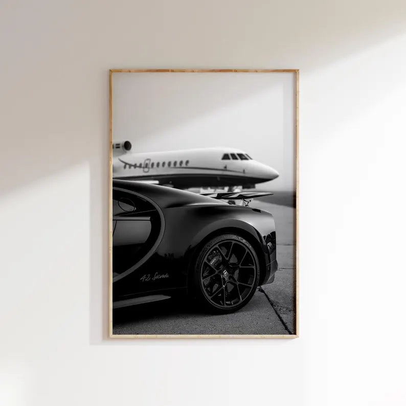 Framed black and white photograph of a car and airplane on a white wall.