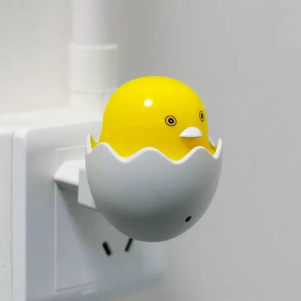 Yellow duckling night light attached to a wall socket on a white background