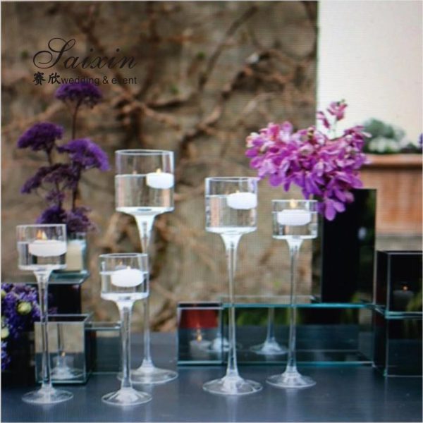 Clear glass candle holders with candles and purple flowers on a blurred background