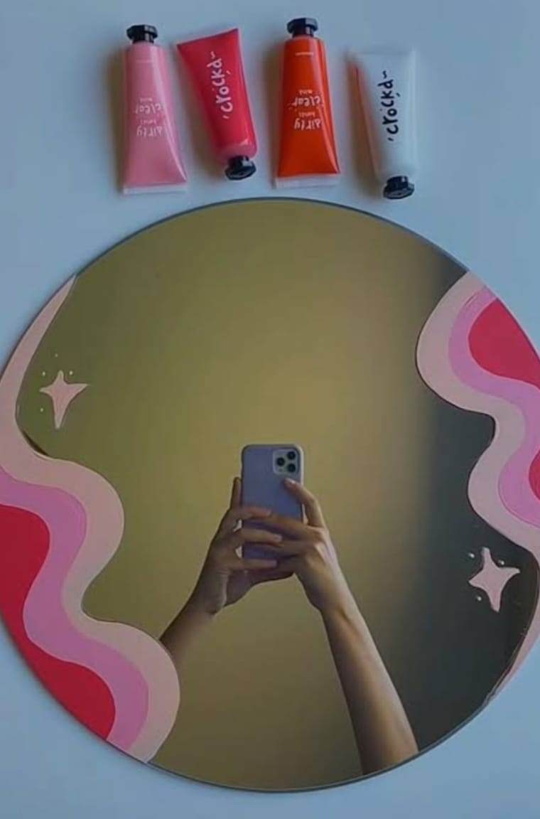 Hand holding a phone taking a mirror selfie with colorful lip products on a pink and red abstract design.