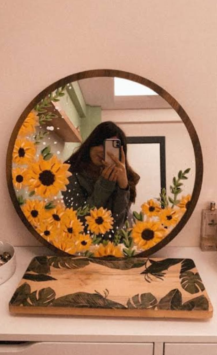 Round mirror with floral design on a wooden stand against a pink wall.