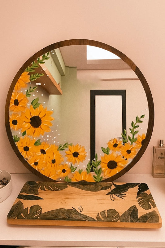 Round mirror with sunflower design on a wooden stand against a pink wall.