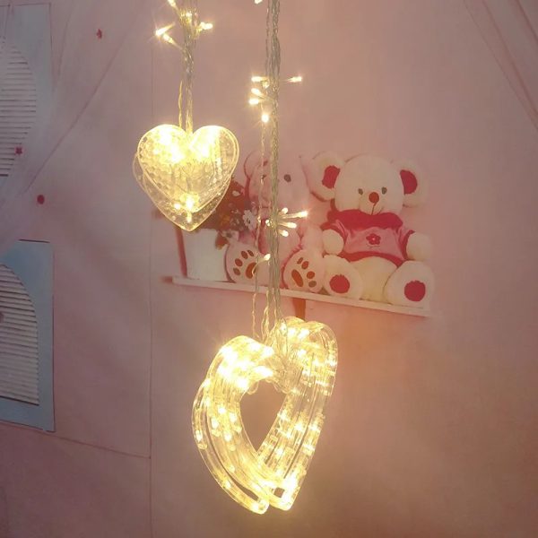 Heart-shaped string lights hanging against a light pink wall with a teddy bear decoration.